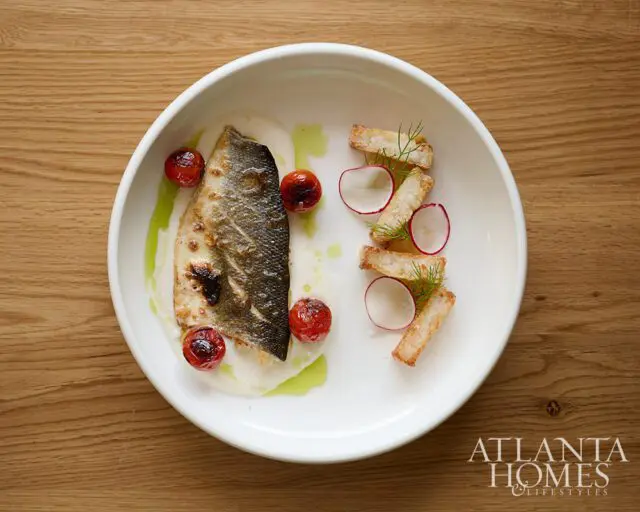Seared fish fillet with roasted cherry tomatoes, radishes, and croutons on a white plate.