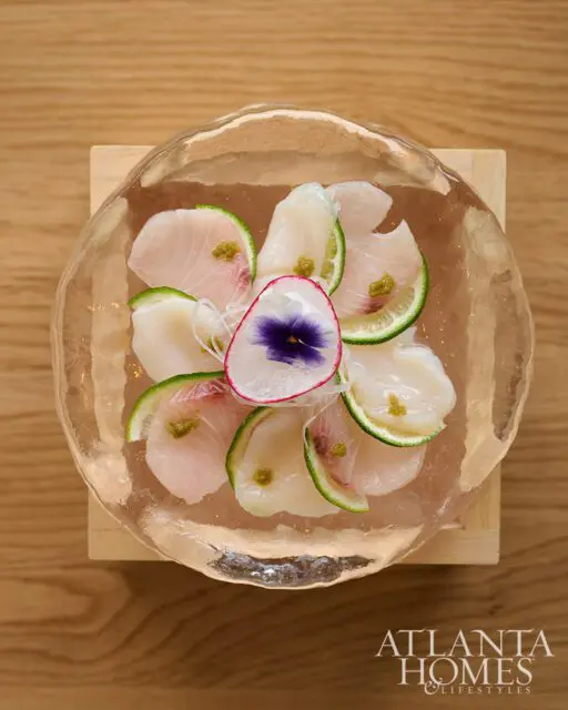 Sashimi with thinly sliced fish, scallops, lime, and edible flower in a clear bowl.