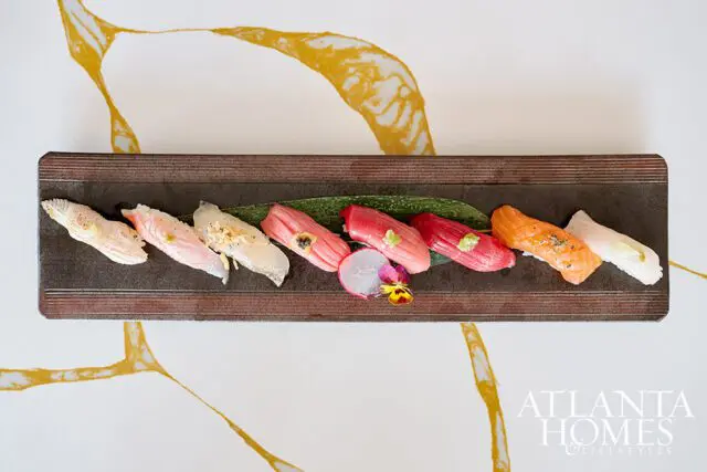 Assortment of sushi on a dark rectangular platter with a leaf garnish.