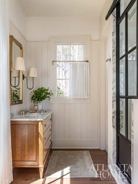 Bathroom with wood vanity, marble countertop, gold mirror, and paneled walls.