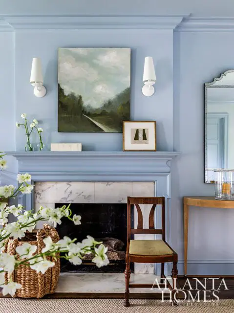 Light blue living room with marble fireplace, landscape painting, and sconces.