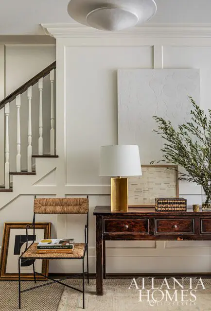 Entryway with dark wood console table, gold lamp, woven chair, and staircase