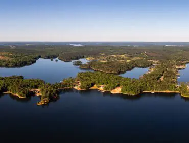 Aerial view of a large lake with wooded peninsulas and scattered homes.