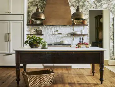 Kitchen island with dark wood base and marble top, brass accents, and pendant lights.