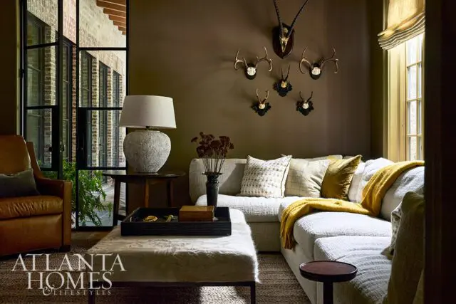 Living room with brown walls, mounted animal antlers, and a sectional sofa with yellow and