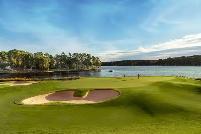 Golf course green with sand traps beside a lake with trees and a boat