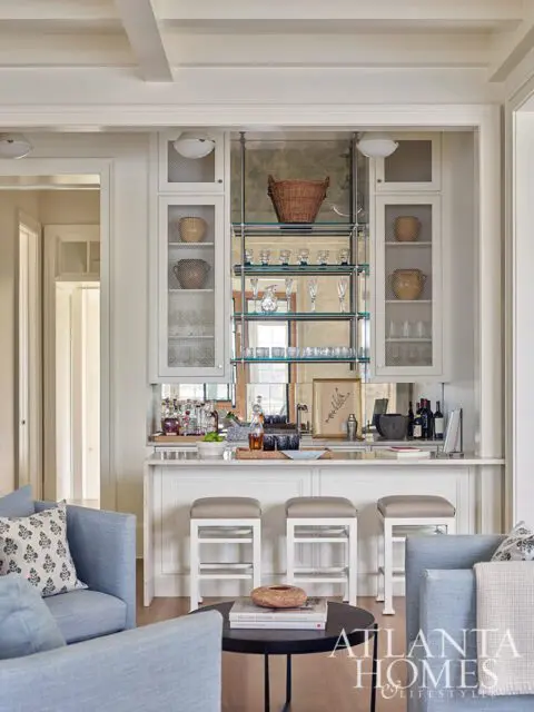 White bar area with mirrored backsplash, glass shelves, and three stools