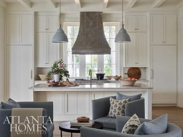 White kitchen with gray pendant lights, metal range hood, and island seating.