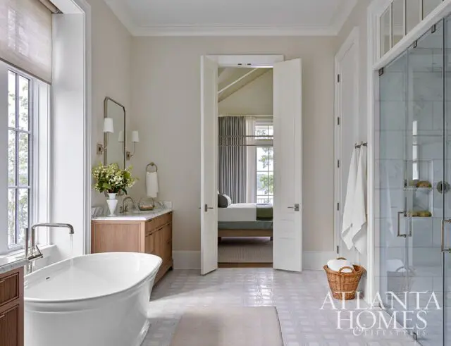 White freestanding tub in a bathroom with wood vanity, marble countertop, and glass shower.