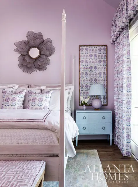 Lavender bedroom with a four-poster bed, floral pillows, a blue dresser, and patterned curtains.
