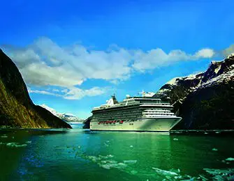 Large white cruise ship sailing through a glacial bay in Alaska with snow-capped mountains