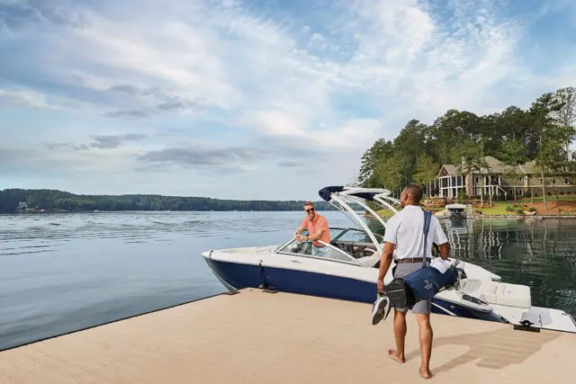 Two men by a boat on a lake with a large house on the shore