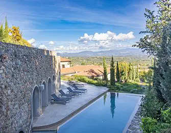 Infinity pool with lounge chairs next to stone wall and Tuscan villa