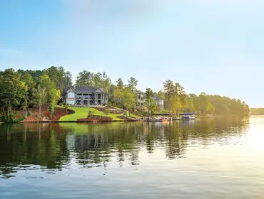 Luxury lake houses with boat docks on a tree-lined shore under a clear sky.