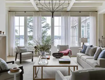 Living room with beige sofa, armchairs, fireplace, and large windows overlooking water