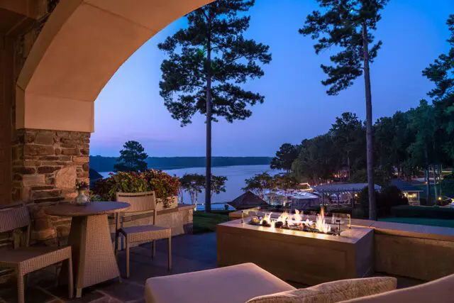 Covered patio with stone accents overlooking a lake at dusk, featuring a fire pit and seating.