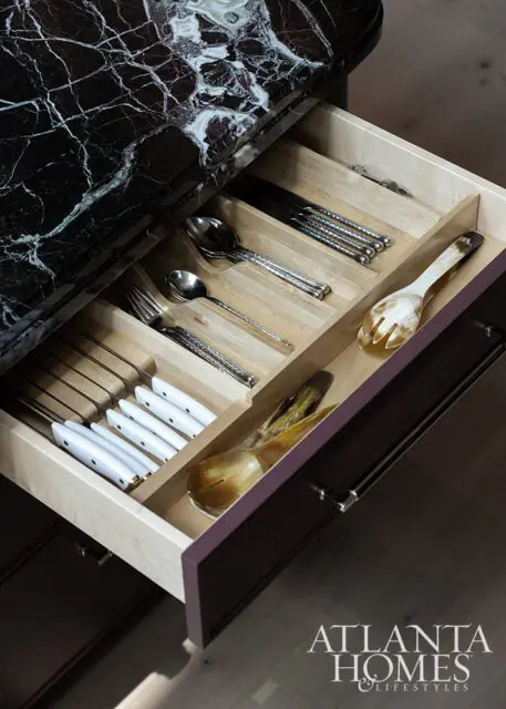 Open kitchen drawer with silverware and serving utensils. Dark marble countertop.