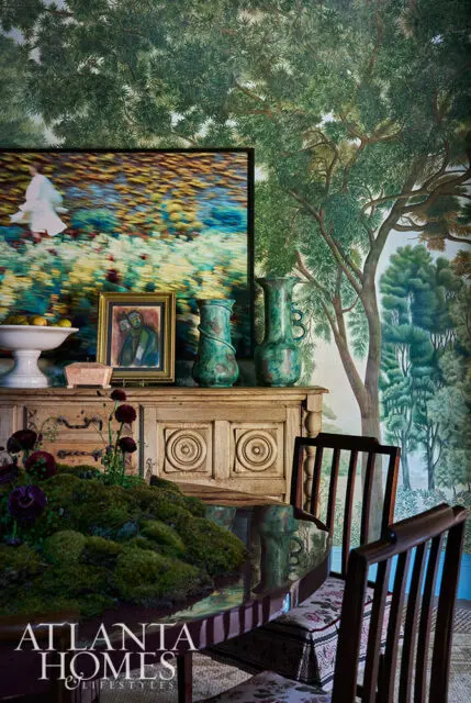 Dining room with forest mural wallpaper, antique buffet, and moss centerpiece on table.
