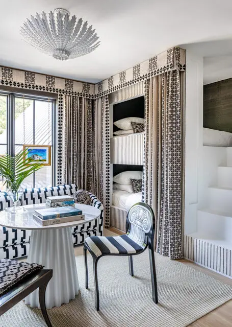Bunk beds with black and white patterned curtains, striped chair, and round table.