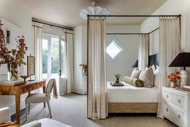 Bedroom with a four-poster bed, patterned ceiling, and a wooden desk with a chair.