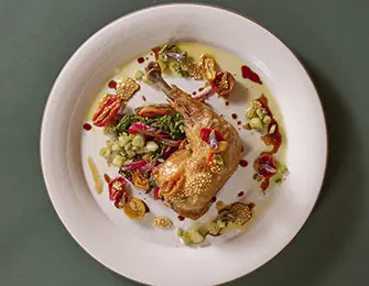 Roasted quail leg with sesame seeds, served with chopped vegetables and dried fruit on a white