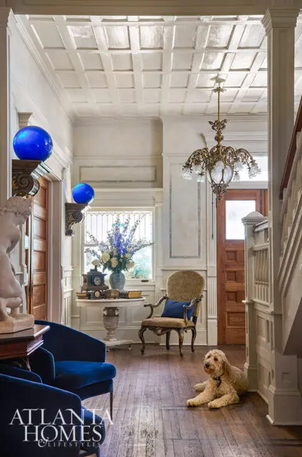 Foyer with blue velvet chairs, ornate chandelier, and dog on hardwood floor.