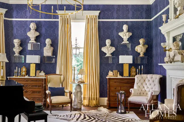 Blue damask wallpaper, classical busts on acrylic shelves, gold curtains, and a zebra rug.