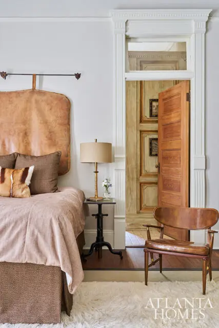 Bedroom with leather headboard, pink bedding, and a leather armchair. Open door reveals ornate