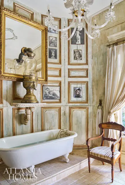 Clawfoot bathtub in a bathroom with paneled walls, ornate mirror, and crystal chandelier.