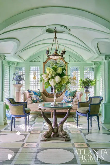 Light green sunroom with arched ceiling, sofa, chairs, and ornate table with dolphin legs.