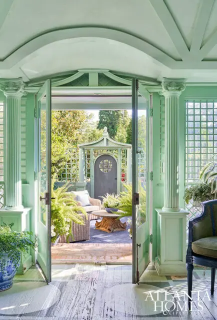 Light green sunroom with double doors opening to a garden gazebo, wicker furniture, and plants.