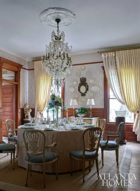Formal dining room with round table, crystal chandelier, and ornate chairs.