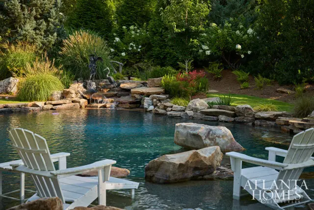 Pool with waterfall, stone landscaping, and two white Adirondack chairs.
