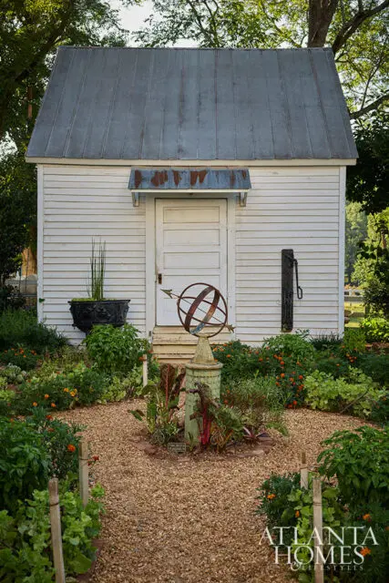 White shed with metal roof, garden path, armillary sphere, and lush garden.