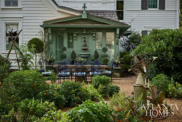 Green garden pavilion with blue chairs around a stone table, sundial, and lush plantings.