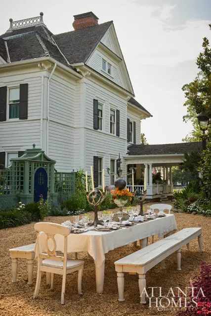 White Victorian house with outdoor dining table set in gravel yard.