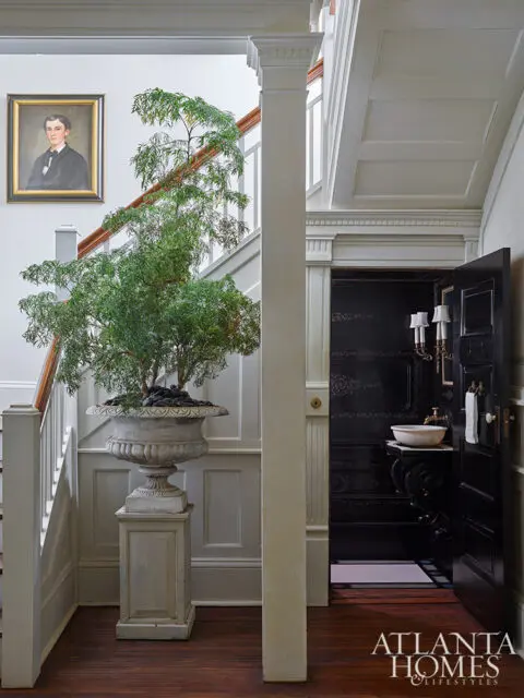 Foyer with staircase, portrait, large potted plant, and black powder room