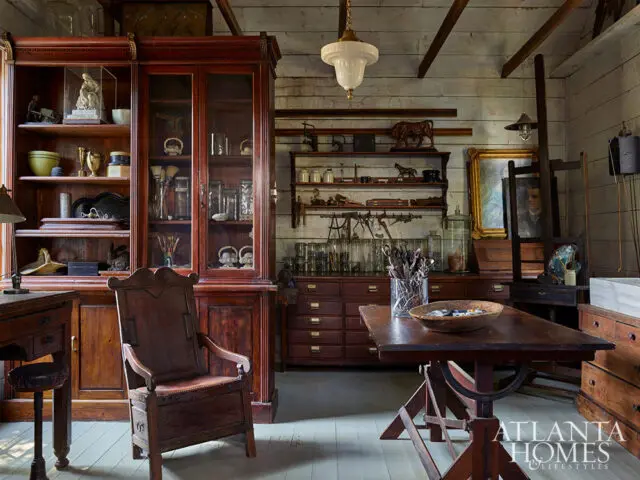 Wooden study with antique furniture, glass-fronted cabinets, and a painting on an easel.