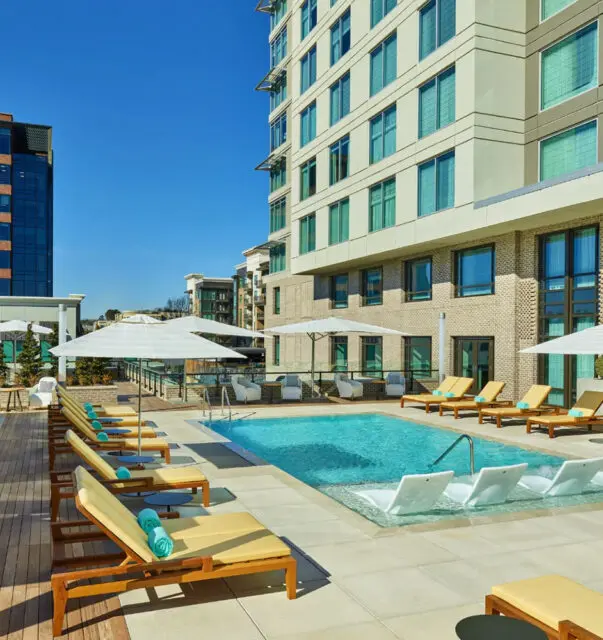 Rooftop pool with lounge chairs and umbrellas next to a modern building.