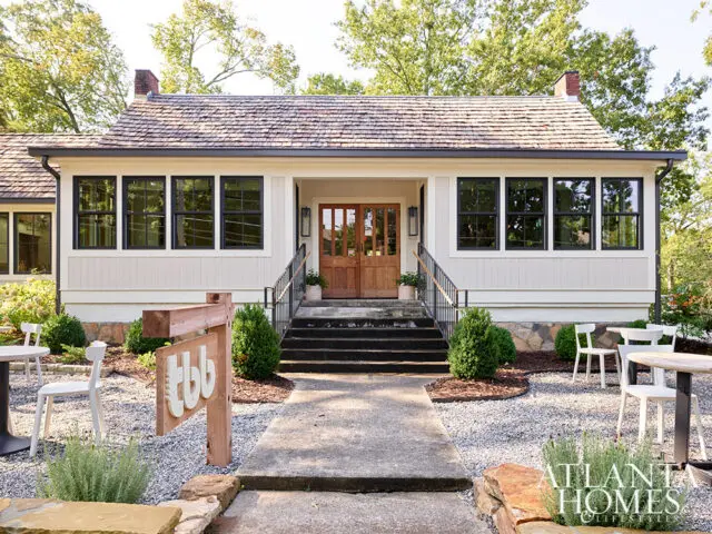 Cream-colored house with wood shingle roof, double wood doors, and black-framed windows.
