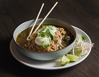 Bowl of noodles with meat, egg, cilantro, lime, and bean sprouts, with chopsticks