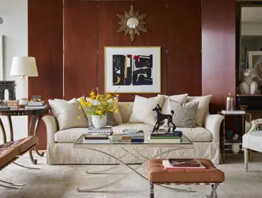 Living room with wood paneled walls, neutral sofa, leather Barcelona chair, and glass coffee table.