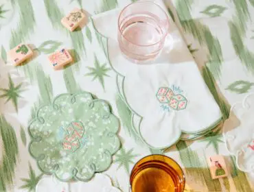 Mahjong tiles and embroidered coasters on a green and white striped tablecloth.