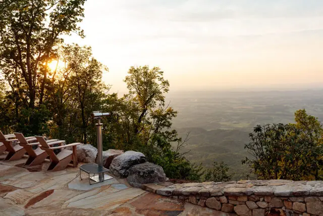 Stone patio with Adirondack chairs and telescope overlooking a valley at sunset