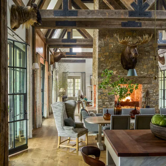 Rustic living room with stone fireplace, mounted moose head, and exposed wooden beams.