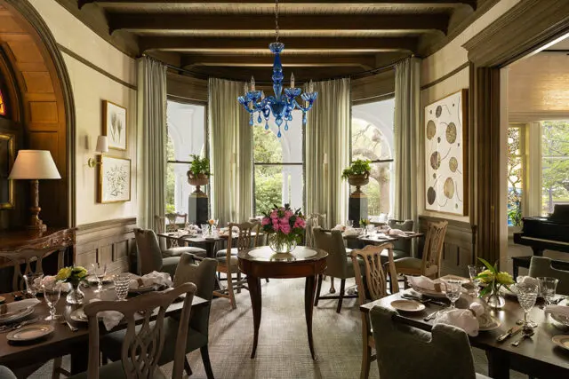 Dining room with tables set for a meal, featuring a blue chandelier and botanical art.