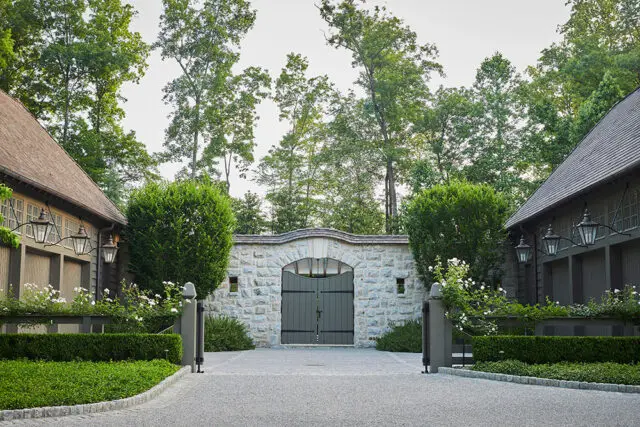 Stone gatehouse with arched double doors, flanked by garages and manicured hedges.
