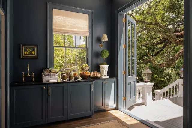Dark blue butler's pantry with brass hardware, black countertop, and view to lush garden.