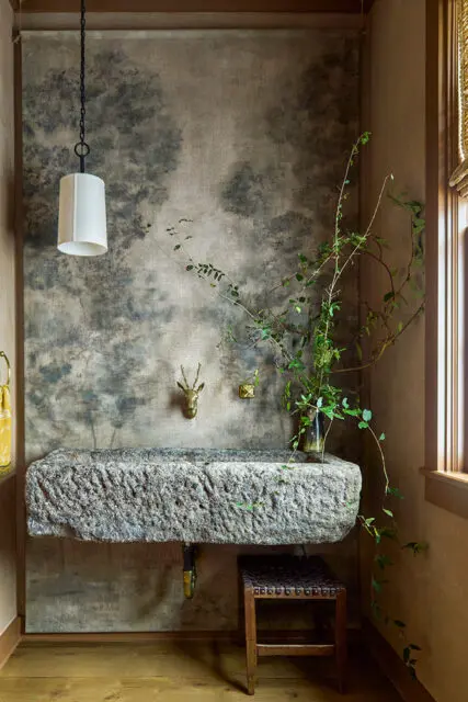Powder room with stone trough sink, deer head wall mount, and forest mural wallpaper.