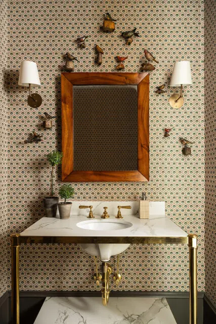 Powder room with patterned wallpaper, marble vanity, brass fixtures, and bird figurines.